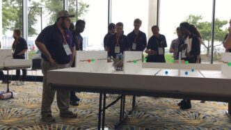 Men standing at table watching robot.