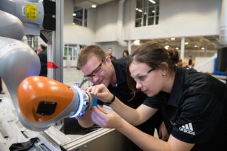 Two students bend over, working on a robotic arm.