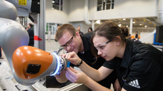Two students bend over, working on a robotic arm.