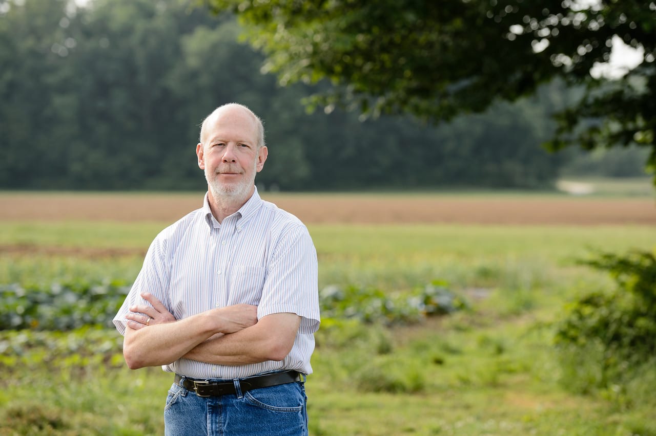 Man stands in green field with arms crossed
