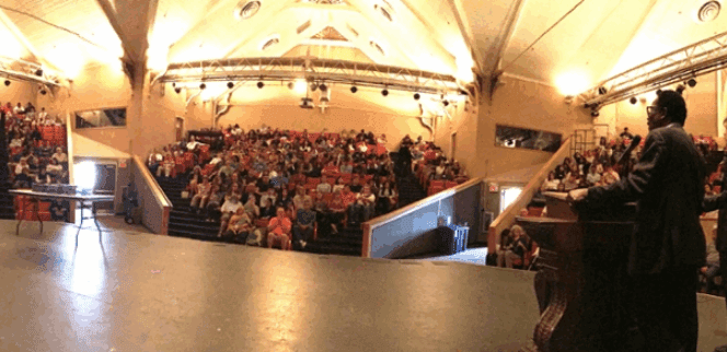 Image of Poetry Declamation juror in front of filled auditorium announcing awards