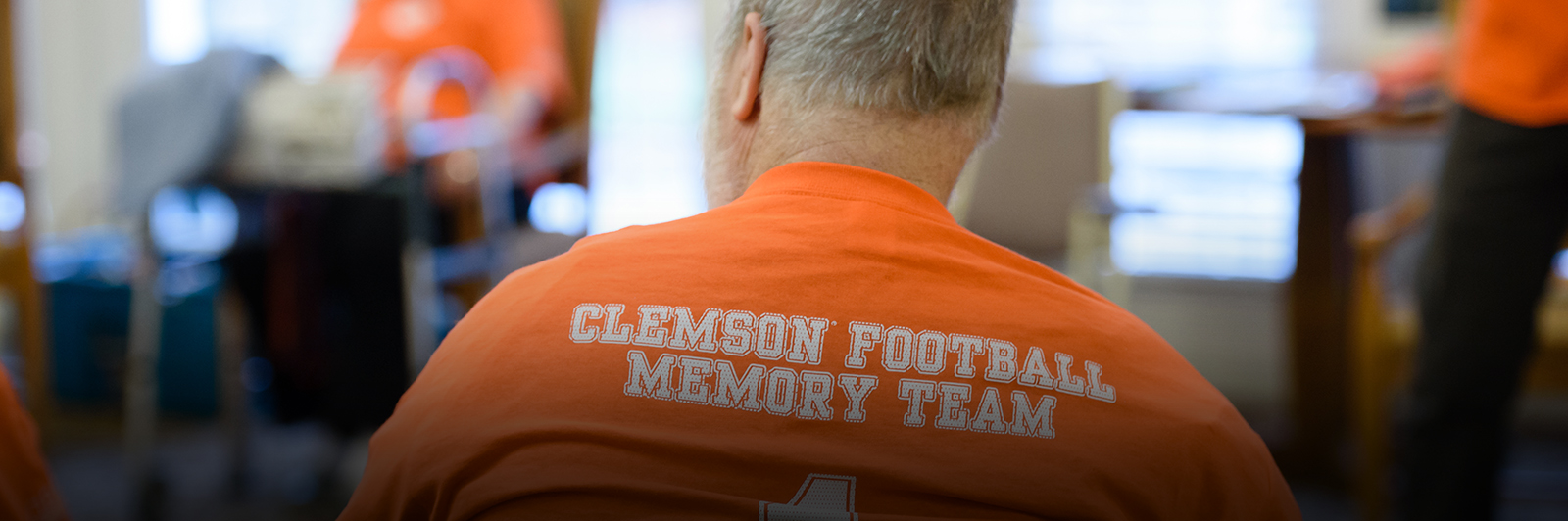 A man's back is shown, with the words "Clemson football memory team" written across the back of his orange shirt.