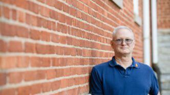 Major Dave Black leans against a brick wall looking into the camera