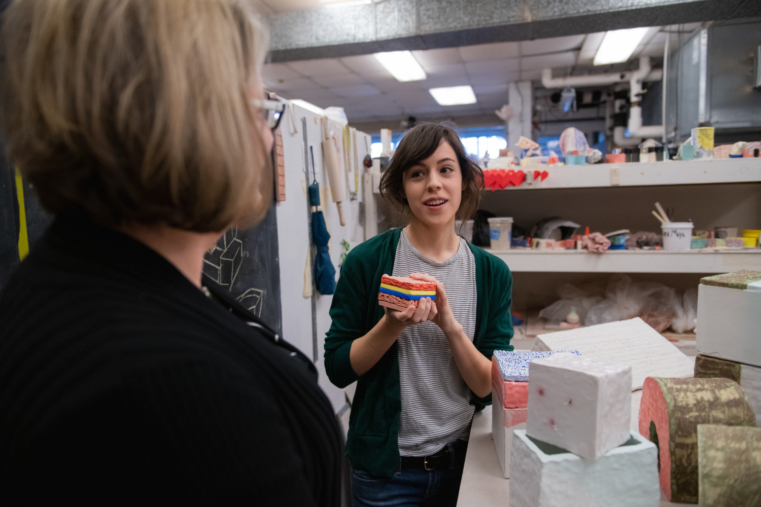 Sara Mays stands in her art studio, surrounded by ceramics work, talking to Valerie Zimany.