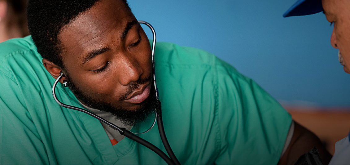 Male Clemson student in green scrubs checks a man's blood pressure.