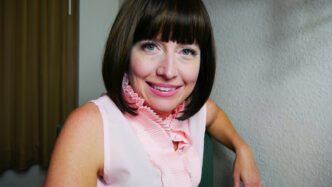 Jillian Weise, head shot, wearing a pink shirt with frilly collar and straight black hair.