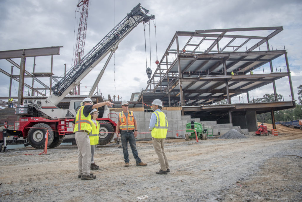 Four people are seen standing at the base of a large building consisting of a steel beam frame.