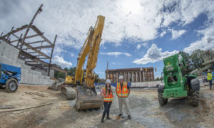 Erin Carpenter and Paul Borick stand in front of large construction equipment with Sirrine Hall and the frame of the new College of Business facility in the background.