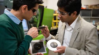 Two men hold automotive parts, inspecting them together.