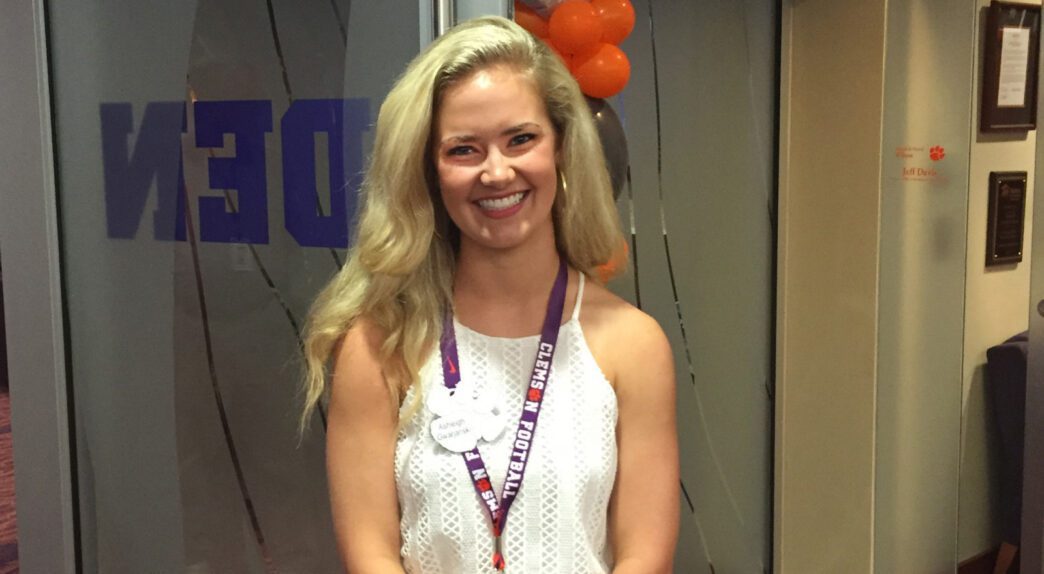 Blonde female student stands in front of a glass wall, posing for a photo.