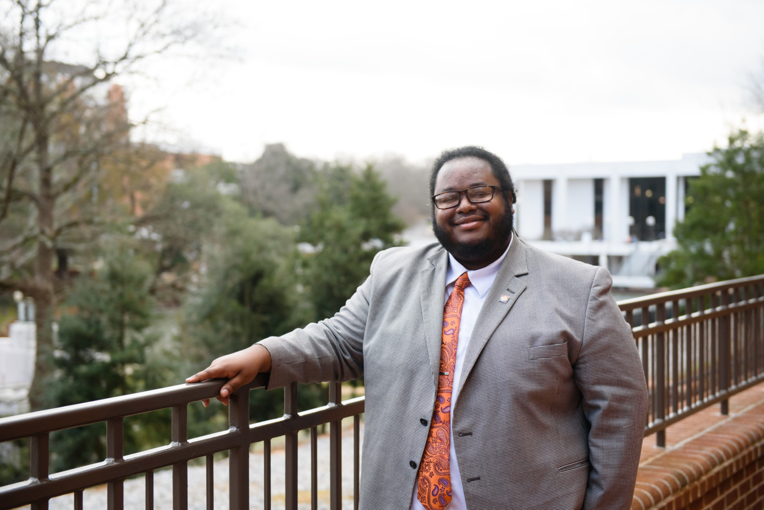 Jerad Green stands with his hand leaning on a metal rail. The Clemson Library is seen in the background.