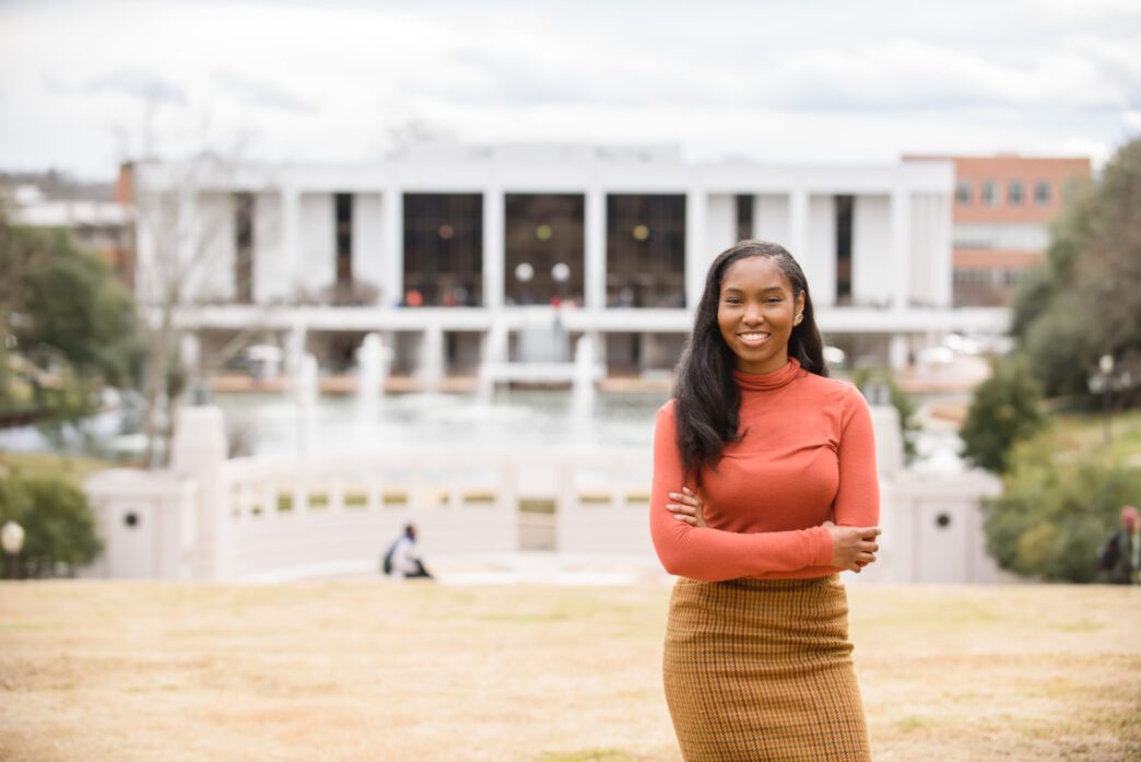 Sarah Dumas stands with her arms crossed with the Clemson R.M. Cooper Library in the background.