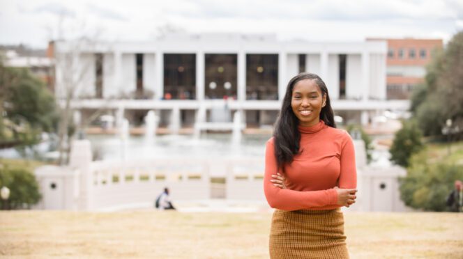 Sarah Dumas stands with her arms crossed with the Clemson R.M. Cooper Library in the background.