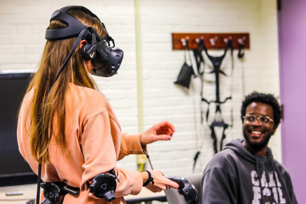 Divine Maloney watches a colleague who is wearing virtual reality goggles.