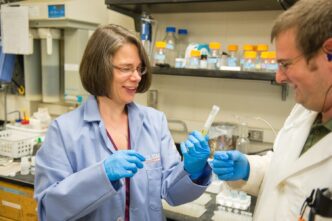 Julia Brumaghim holds pipets in her lab while a colleague stands to her right.
