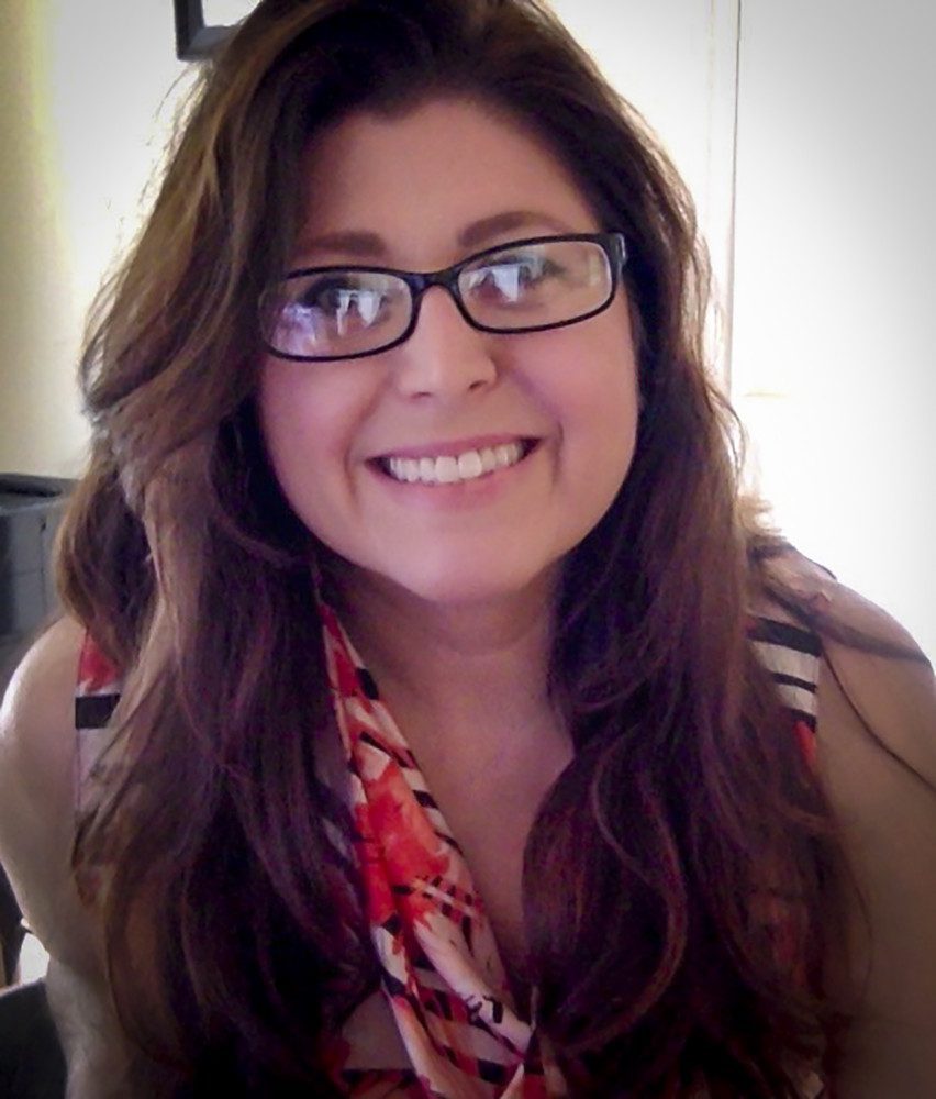 A pretty woman with long brown hair and glasses smiles at the camera