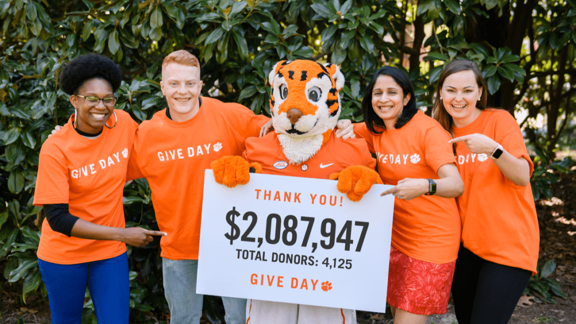 Clemson students and faculty stand with the cub holding a sign with total amount raised.