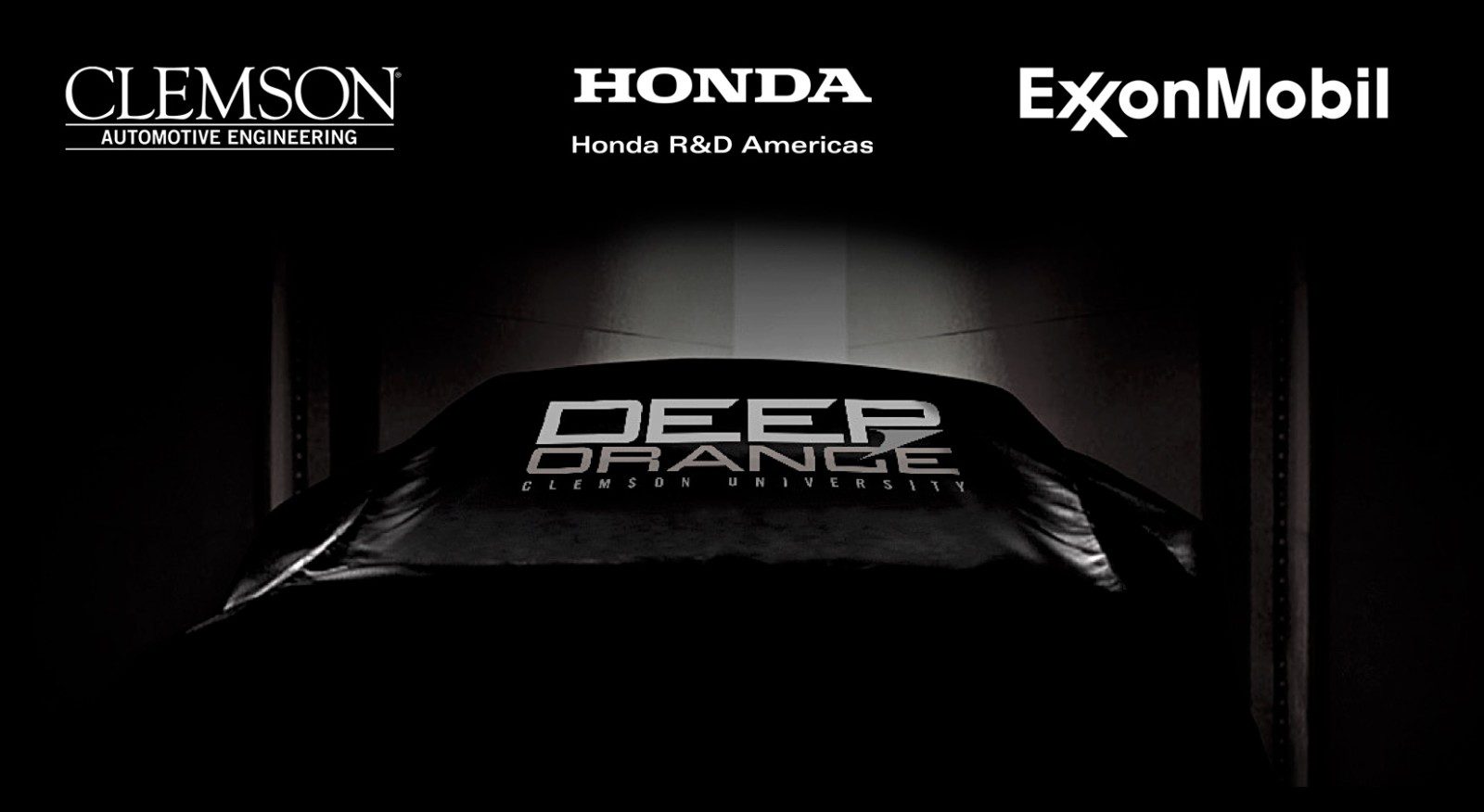 Black and white image of car covered with protectant cover that says DEEP ORANGE. University, Honda and Exxon logos are across the top.