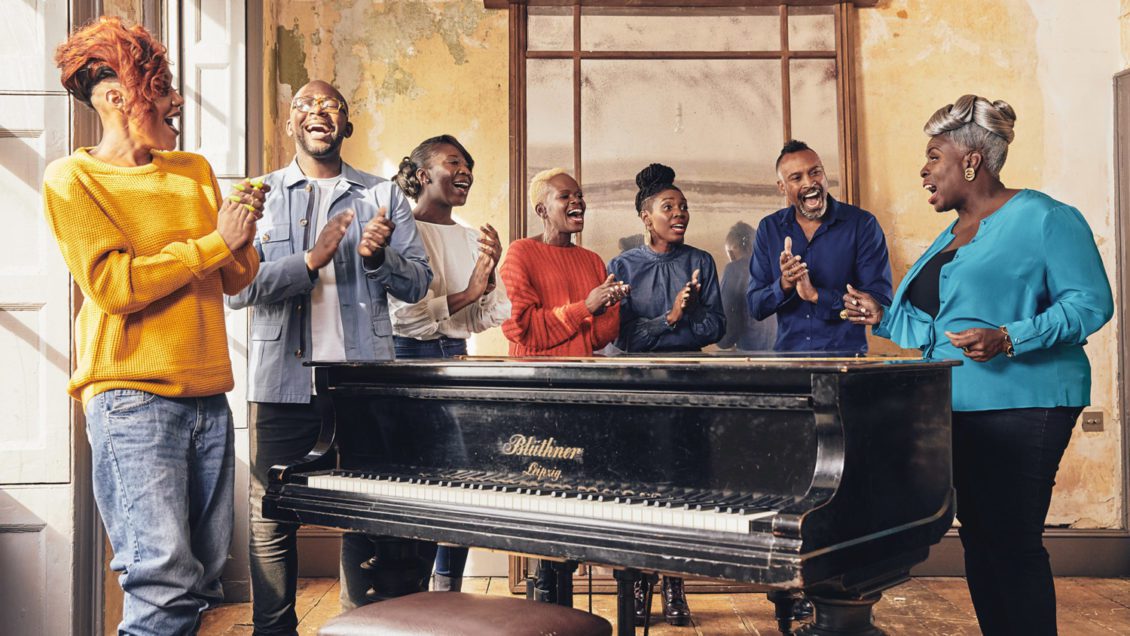 Members of the Kingdom Choir stand in a semi-circle around a piano and sing.
