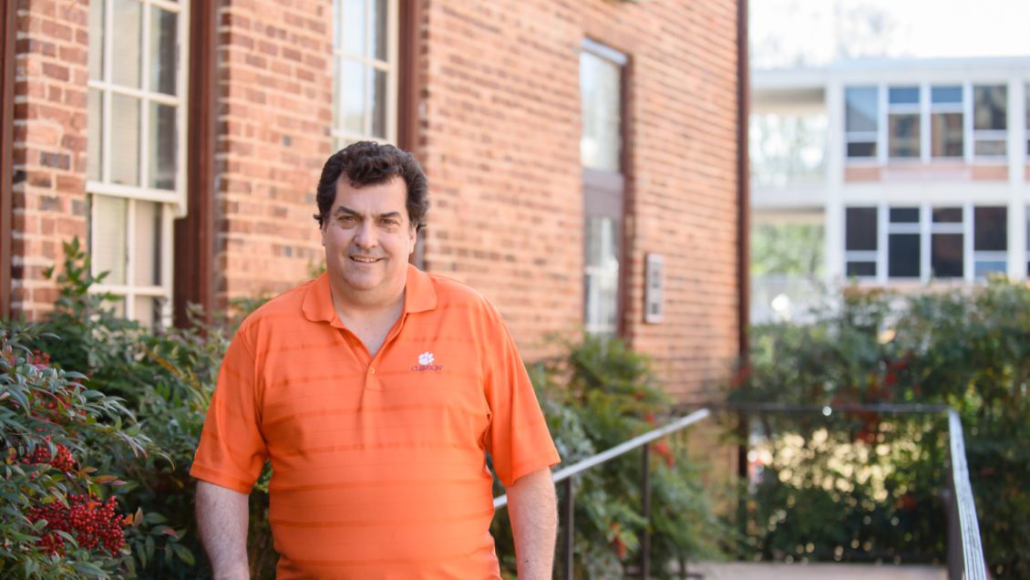 Michael Childress leans against a handrail outside a brick building on Clemson's campus.