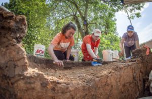 three students dig in the dirt from their knees