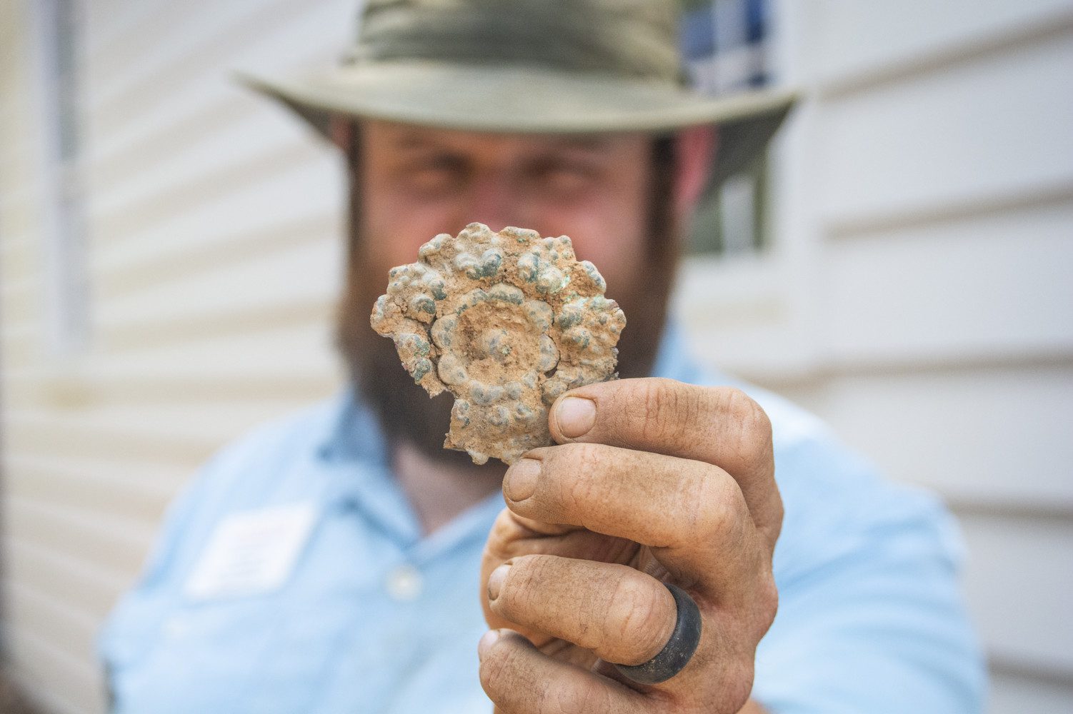 A man holds up a decorative round piece of brass, with dirt all over it and his hands