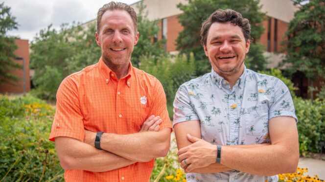 Two men stand with their arms crossed, smiling for the camera