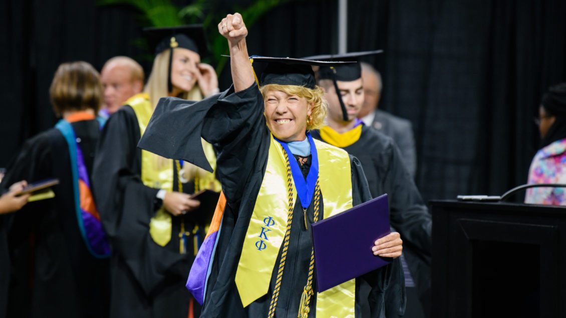 Paige Zoltewicz smiling big while awaiting to shake President Jim Clements' hand at August 2019 graduation.
