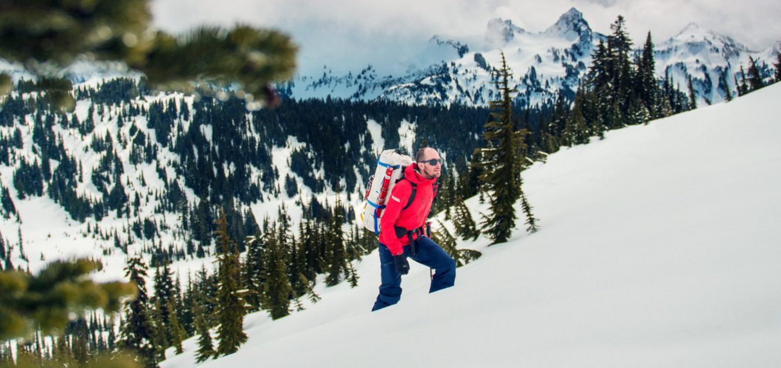 Man in red jacket climbs up a snow-covered mountains