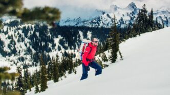 Man in red jacket climbs up a snow-covered mountains