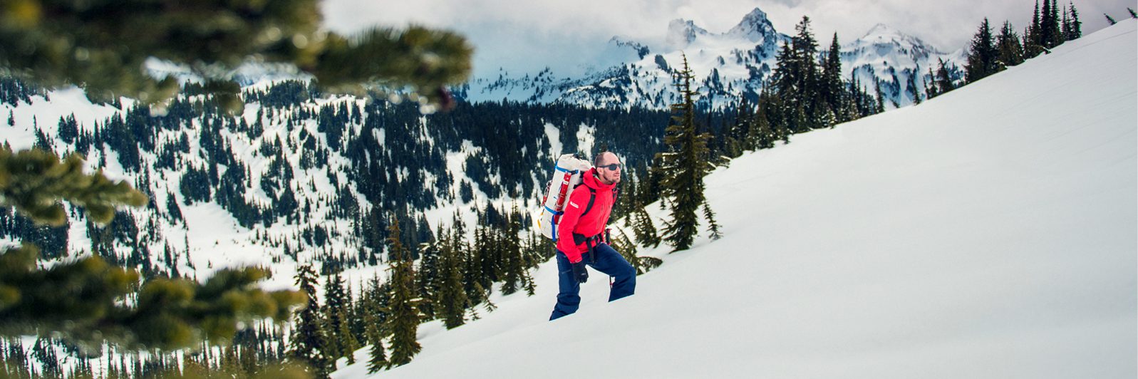Man in red jacket climbs up a snow-covered mountains