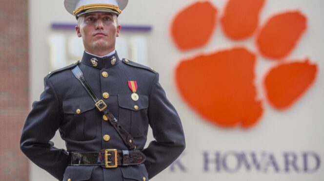 A Marine in dress uniform stands with arms behind his back, a large Clemson Tiger paw attached to Memorial Stadium behind him, over his shoulder