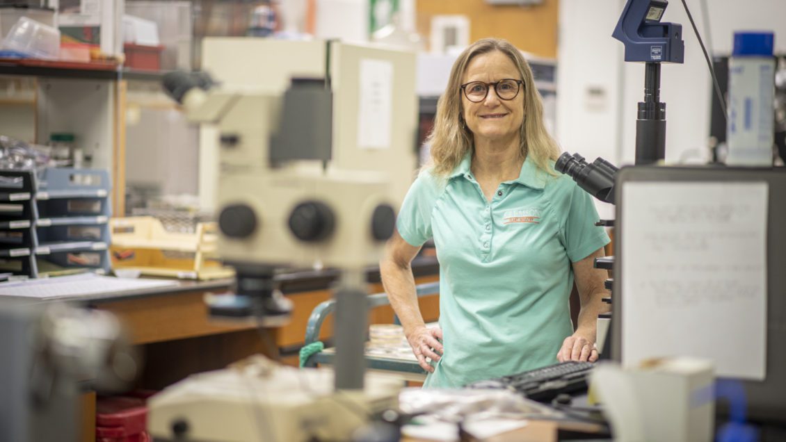 A woman in a sea green shirt smiles at the camera behind a table full of scientific equipment