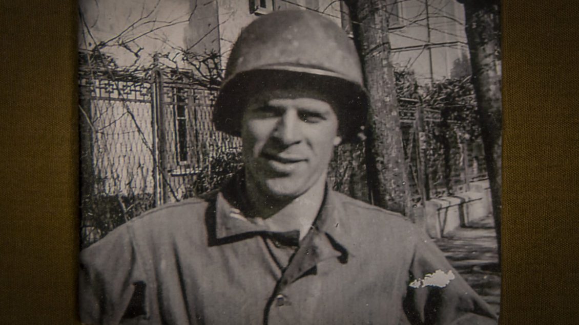 A black and white photo of a man in WWII Army uniform and helmet