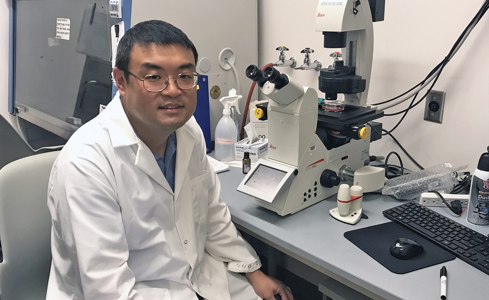 Zhicheng Dou sitting at microscope in his lab