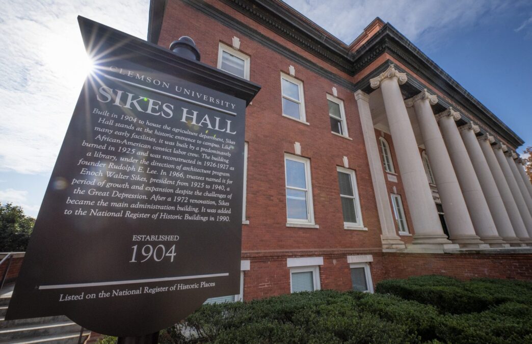 The sun flares over the edge of a sign in front of Sikes Hall