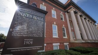 The sun flares over the edge of a sign in front of Sikes Hall
