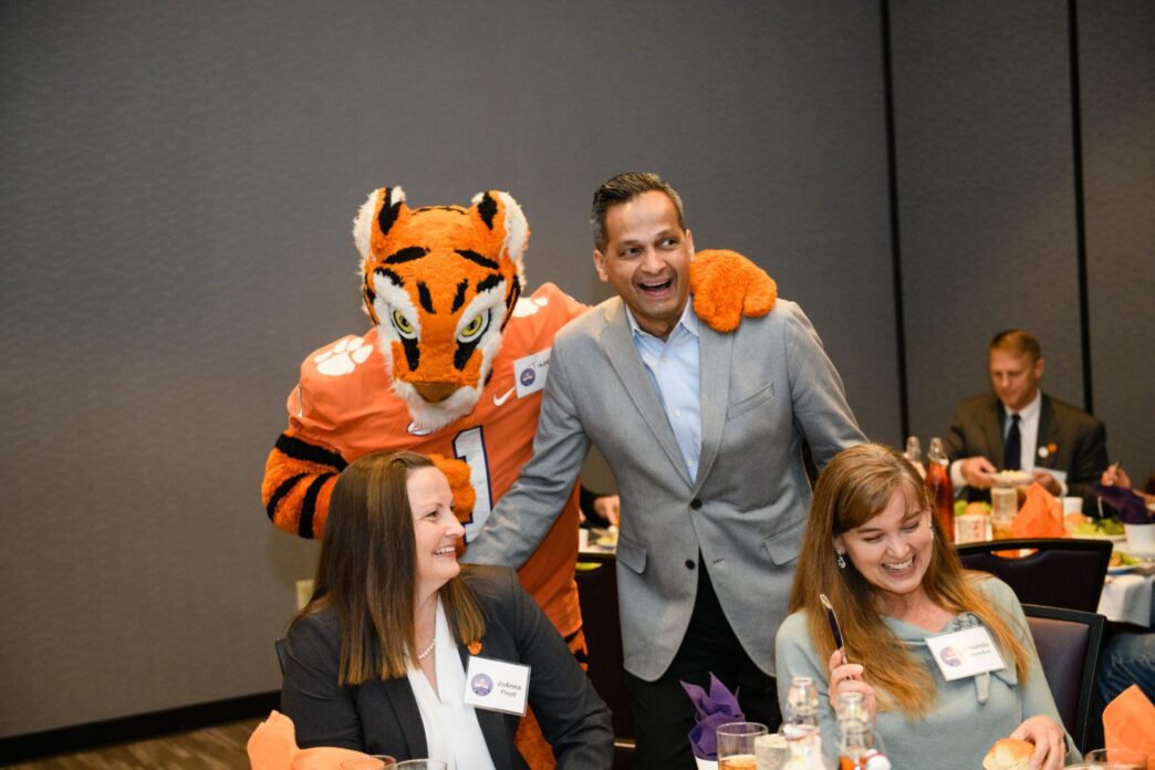 A man and a woman laugh as they greet the school mascot.