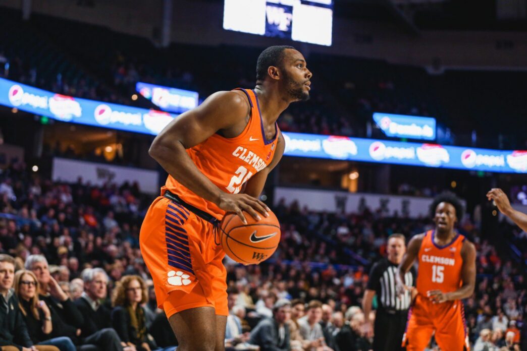 A basketball player stands with the basketball looking to shoot or pass the ball.