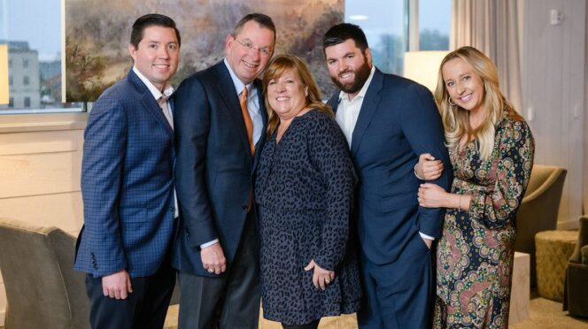 Five people, Mitch, Carla, two sons, and one daughter-in-law, pause for a family photo.