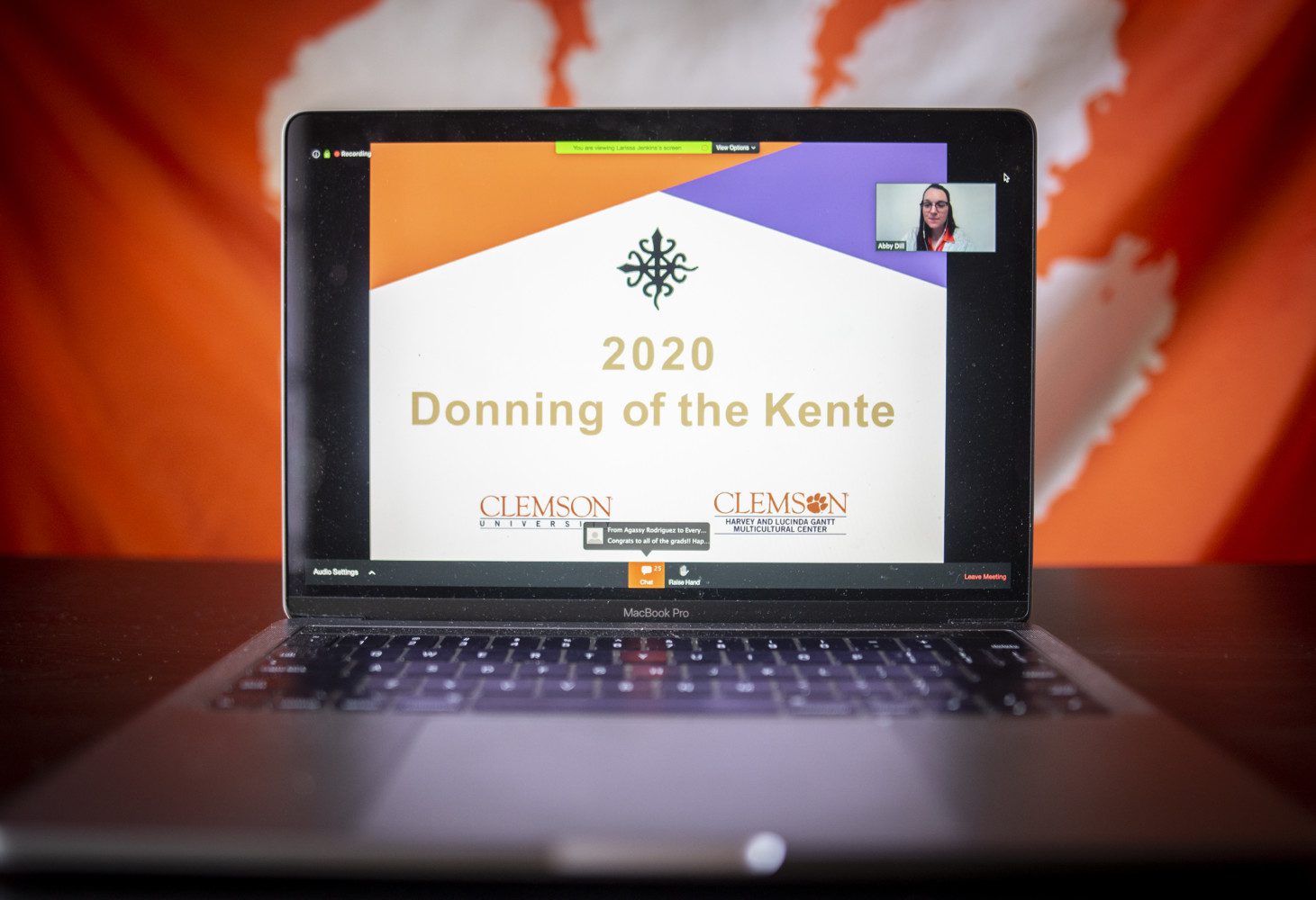 A laptop sits on a table with the Donning of the Kente ceremony home screen open