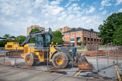 A tractor sits inside of a fenced construction zone in front of a brick building.