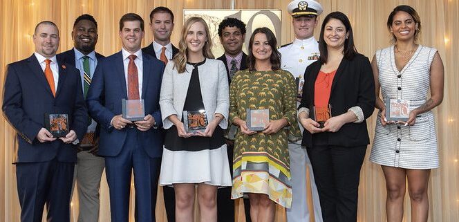 A group of men and women stand side-by-side holding trophies