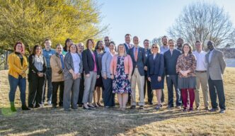 A group of about 20 people stand on a lawn smiling at the camera
