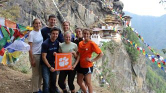 A group of students standing on a cliff on the side of a mountain holding a square tiger rag with the Clemson paw on it