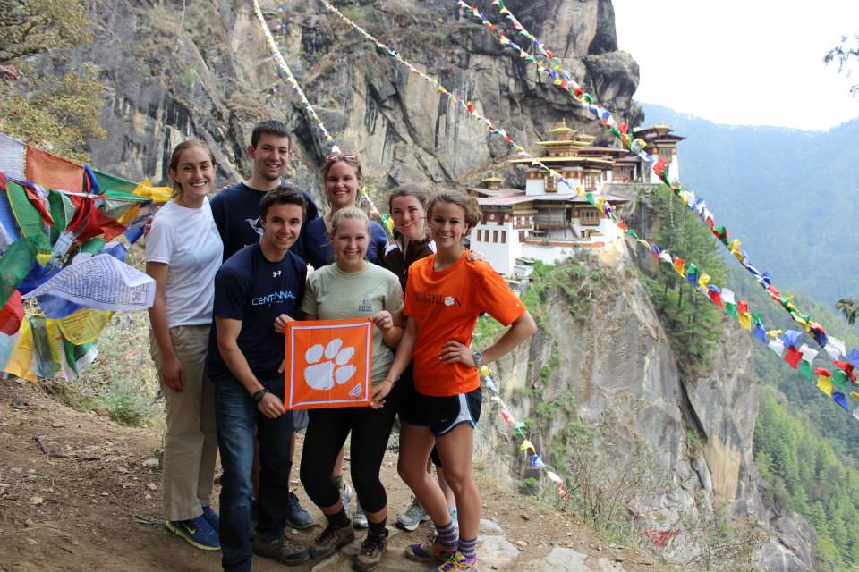 A group of students standing on a cliff on the side of a mountain holding a square tiger rag with the Clemson paw on it
