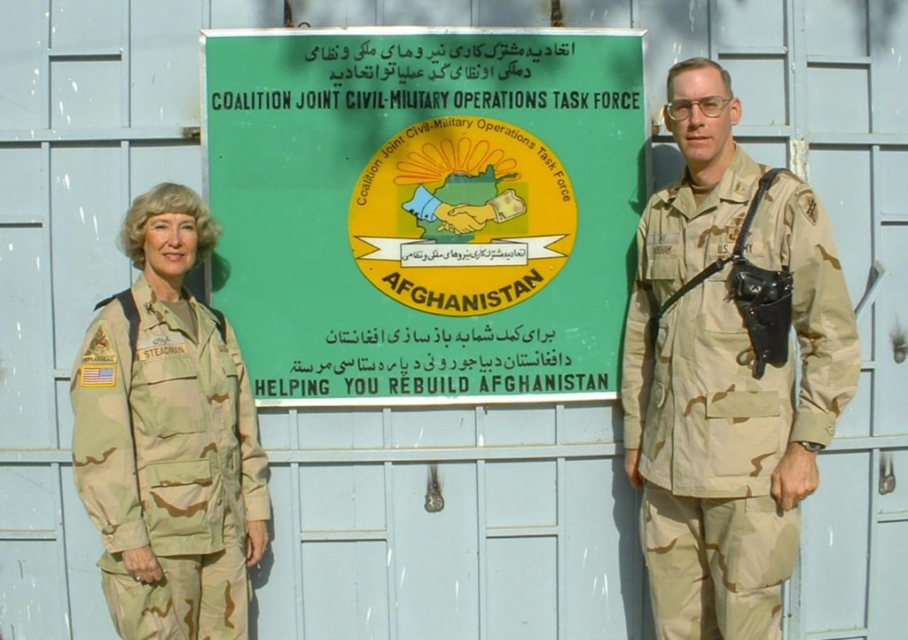 Two Army officers stand on either side of a green sign