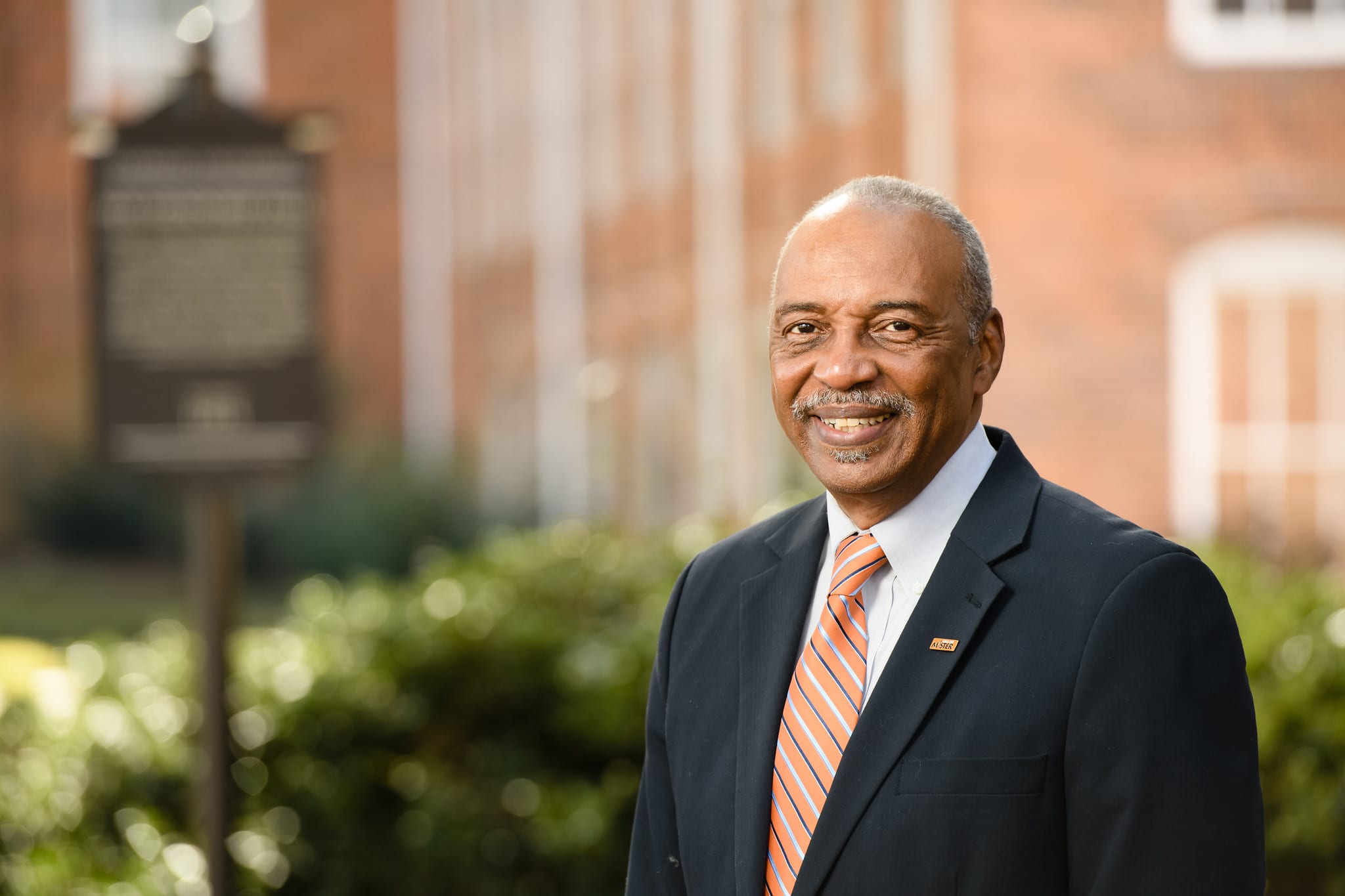Man in suit in front of brick building.