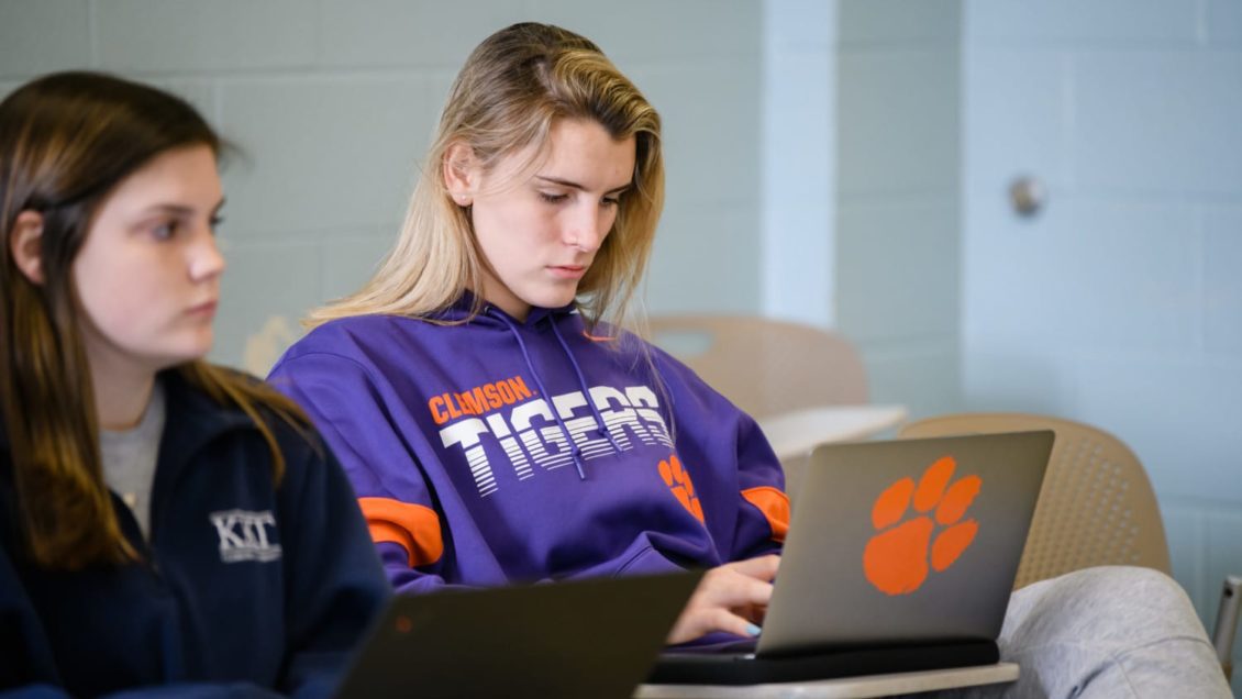 A Clemson student types on a laptop inside a classroom