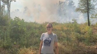Crystal Smith standing in the woods with smoke behind her.